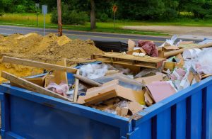 Industrial dumpster bin blue construction debris container filled with rock and concrete rubble.